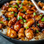 Close-up of glazed honey BBQ chicken chunks over rice, topped with green onions