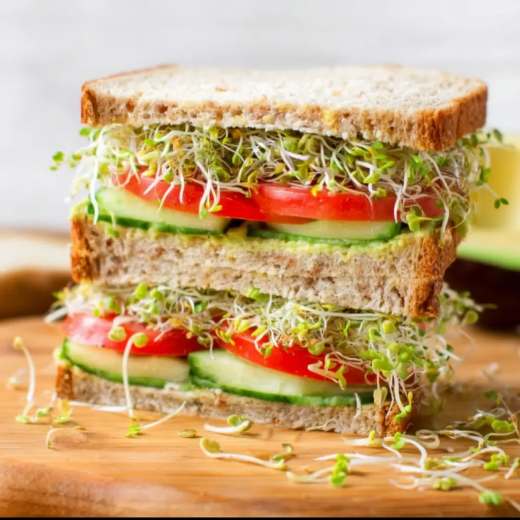 Vegan sandwich with avocado, tomato, cucumber, and sprouts on whole grain bread, stacked and cut in half